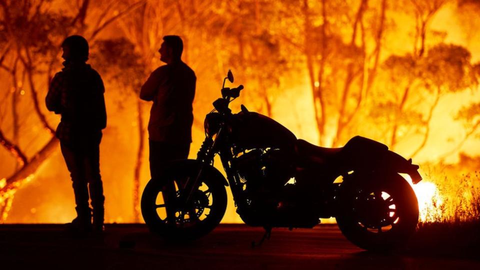 El cielo se enrojeció y oscureció varias zonas del sudeste de Australia a medida que las ráfagas de viento exacerbaban el fuego, en una de las peores temporadas de incendios forestales en el país. Aquí, un par de residentes de Tabourie Lake, a unos 200 kilómetros al sur de Sídney, observan cómo las llamas se devoran un bosque.