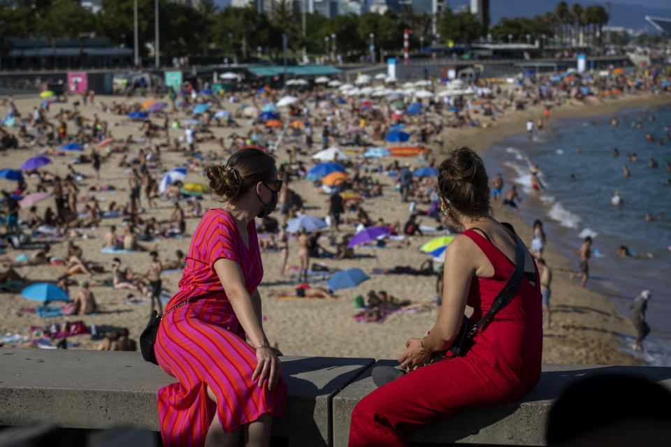 Two women look at the beach in Barcelona, Spain, Saturday, July 18, 2020. Police in Barcelona are closing access to a large area of the city's beaches due to the excess of sunbathers who decided to ignore the urgings of authorities to stay at home amid a resurgence of the coronavirus. (AP Photo/Emilio Morenatti)