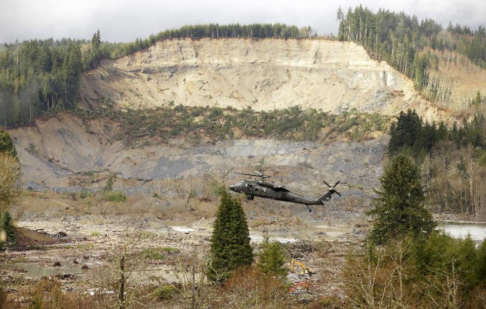 A military helicopter flies Thursday, March 27, 2014, over mud and debris from the massive mudslide that struck Saturday near Darrington, Wash. Search and recovery work continued throughout the day. (AP Photo/Ted S. Warren, Pool)