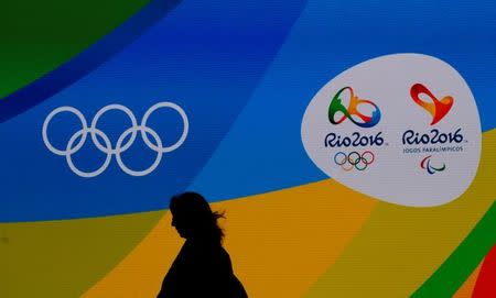 A journalist walks in front of a screen with Olympics logos during the medal launching ceremony in Rio de Janeiro, Brazil, June 14, 2016. REUTERS/Sergio Moraes
