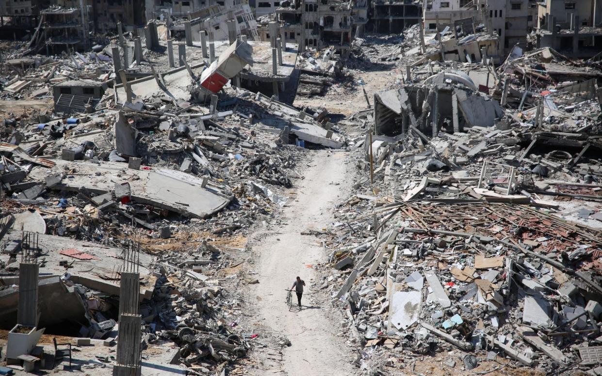 A man pushes a bicycle amid buildings transformed to rubble in the devastated area around Gaza's Al-Shifa hospital