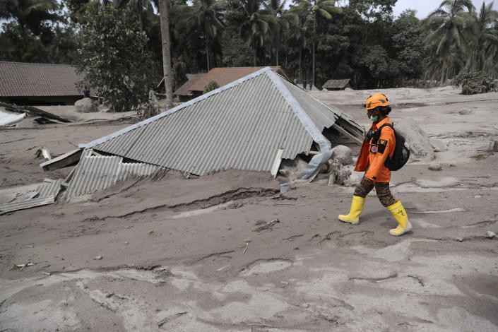 A rescuer walks past a house buried in the ash following the eruption of Mount Semeru in Lumajang district, East Java province, Indonesia, Sunday, Dec. 5, 2021. The death toll from eruption of the highest volcano on Indonesia's most densely populated island of Java has risen with scores still missing, officials said Sunday as rain continued to pound the region and hamper the search.(AP Photo/Trisnadi)