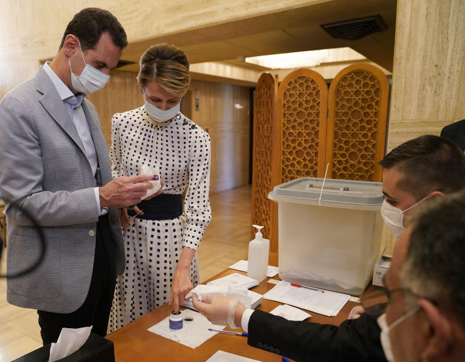 FILE - This file photo released July. 19, 2020 on the official Facebook page of Syrian Presidency, shows Syrian President Bashar Assad, left, and his wife Asma voting at a polling station in the parliamentary elections, in Damascus, Syria. The office of Syrian President Bashar Assad said Monday, March 8, 2021 that Assad and his wife have tested positive for the coronavirus and are both doing well. In a statement, Assad's office said the first couple did PCR tests after they felt minor symptoms consistent with the COVID-19 illness. (Syrian Presidency via AP, File)