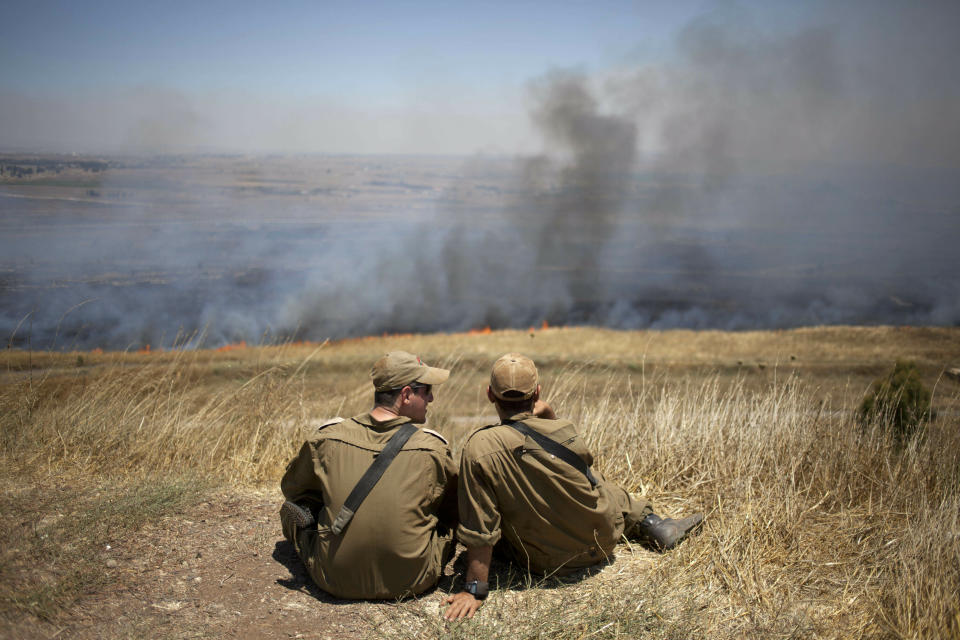 FILE - In this July 16, 2013, file photo, Israeli soldiers sit in a position on the border with Syria on the Israeli-controlled Golan Heights as smoke rises following explosions of mortar shells. President Donald Trump’s move to recognize Israeli sovereignty over the Golan Heights turns the tables on decades of U.S. diplomacy and international law and threatens to further inflame regional tensions. (AP Photo/Ariel Schalit, File)