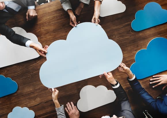 Business team holding cutouts of clouds in office; symbolic cloud computing meeting.