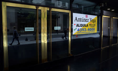 People are seen reflected as they walk past an out-of-business store in Buenos Aires' financial district, Argentina October 18, 2018. Picture taken October 18, 2018. REUTERS/Marcos Brindicci