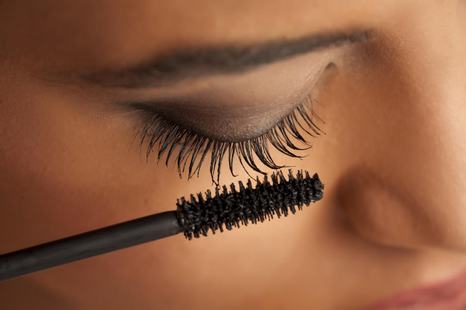 Eine junge Frau trägt schwarze Mascara auf ihre Wimpern auf