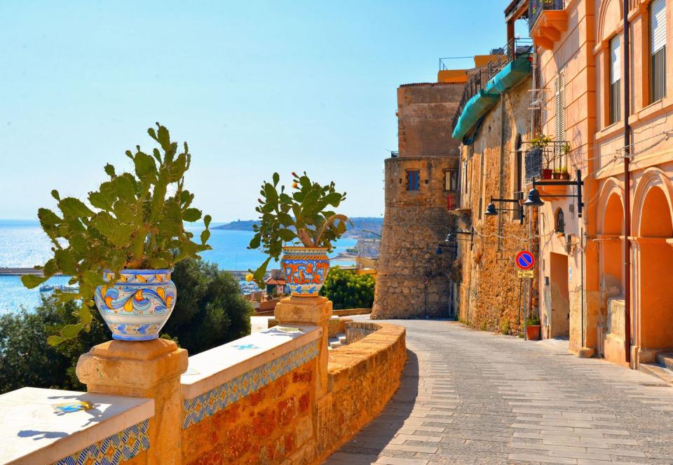 old narrow street with ceramic pot with cactus on wall and view on the port and sea in front of sciacca, sicily, italy