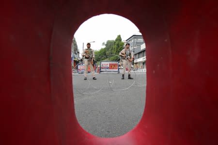 Indian security personnel stands guard behind a roadblock along a deserted street during restrictions in Jammu