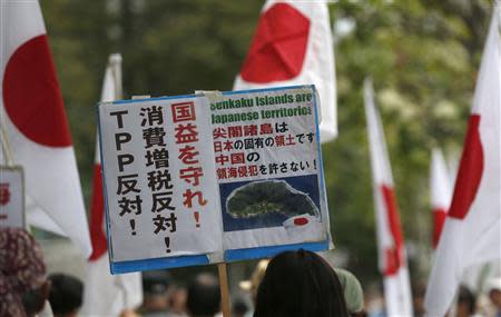 A member of the nationalist movement "Ganbare Nippon" holding a placard of disputed islands known as Senkaku in Japan and Diaoyu in China, walks among Japanese national flags during a rally in Tokyo September 11, 2013, on the day of one year anniversary of Japanese government signed contract to buy islands disputed with China from a private owner. REUTERS/Toru Hanai