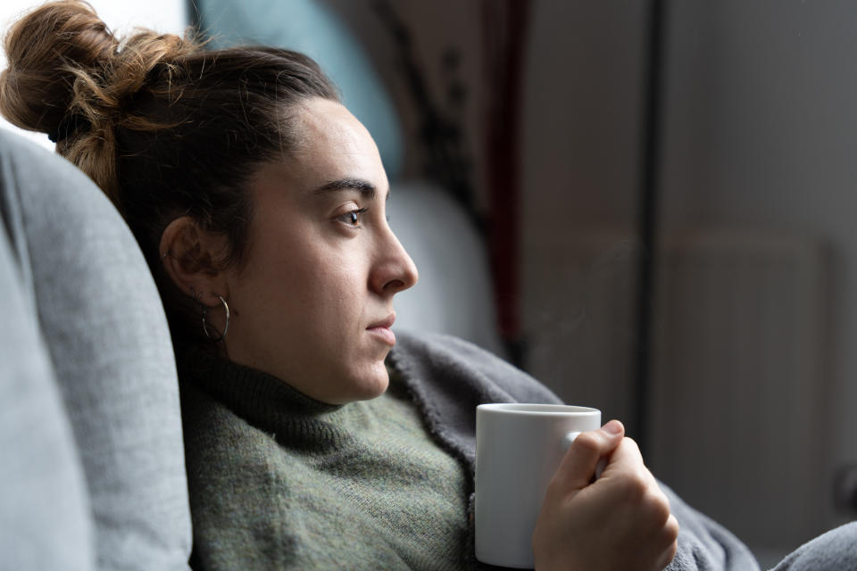 Concerned young woman holding a warm cup of coffee on couch
