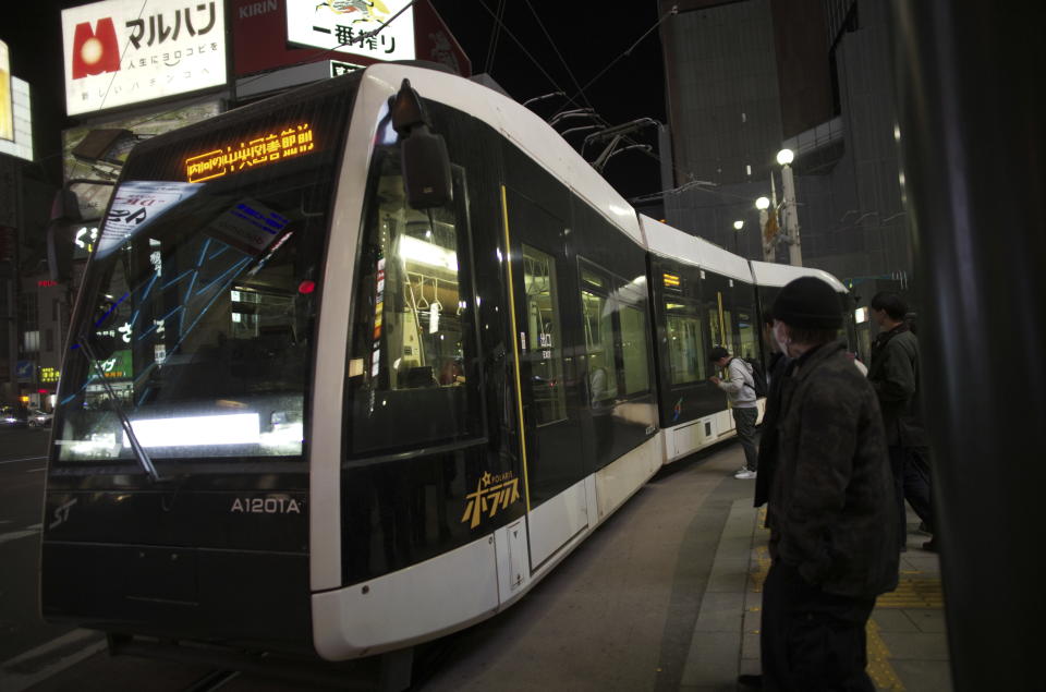 A tram moves through a traffic light as people wait for the light to turn green in the Susukino district of Sapporo, northern Japan, Friday, April 14, 2023. G-7 energy and environment ministers are meeting in the city on the northern Japanese island of Hokkaido ahead of a summit next month. (AP Photo/Hiro Komae)