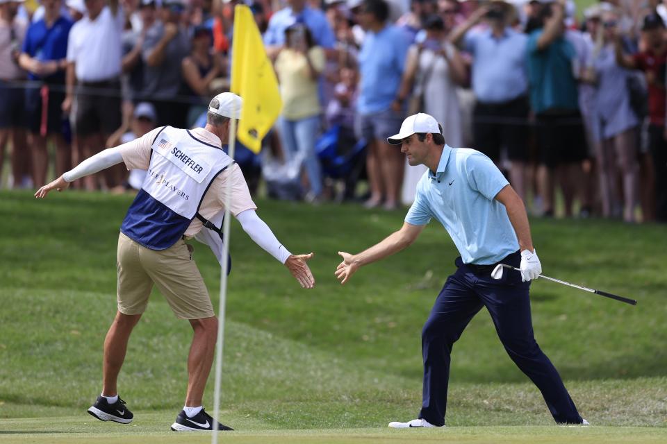 Scottie Scheffler slaps palms with caddie Ted Scott after chipping in for birdie at the par-3 eighth hole of the Players Stadoum Course during the final round of The Players Championship on Sunday.