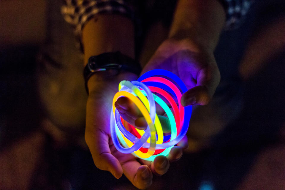 An outstretched pair of hands holds several intertwined neon bracelets.