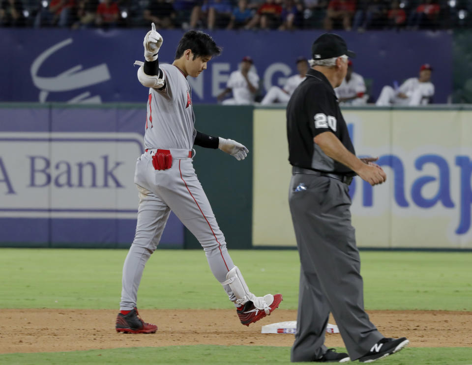 Los Angeles Angels' Shohei Ohtani gestures to the dugout after hitting an RBI double, next to umpire Tom Hallion (20), during the eighth inning of the team's baseball game against the Texas Rangers in Arlington, Texas, Tuesday, Aug. 20, 2019. (AP Photo/Tony Gutierrez)