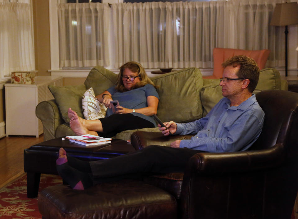 In this Sept. 25, 2018, photo, Barb Hailey, left, checks her phone while her husband, Allen Hailey watches TV in their Chicago home. Like a lot of parents, they use their phones for work and fun, something their boys like to point out when they try to limit the boys' screen time. (AP Photo/Martha Irvine)