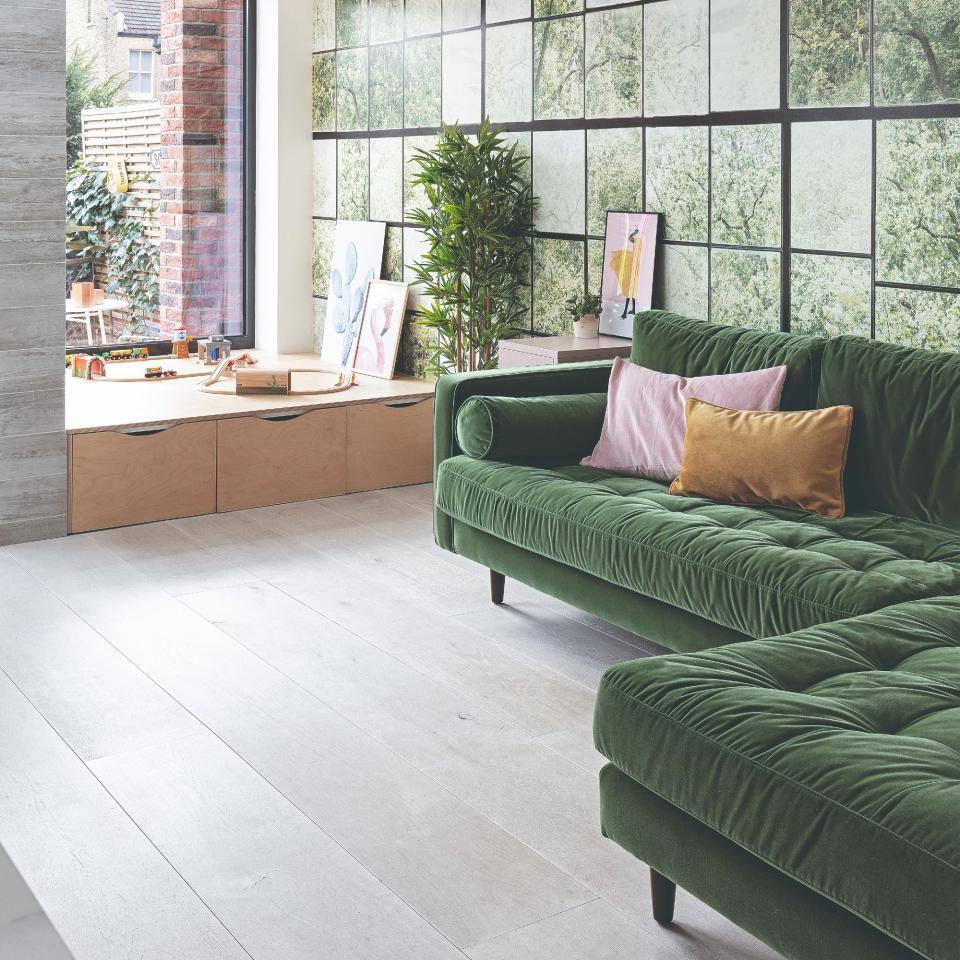 Green corner sofa in a living room with large windows