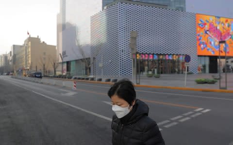  A Chinese woman wears a mask as she walks in an empty street after Chinese New Year celebrations were cancelled in Beijing, - Credit: Rex