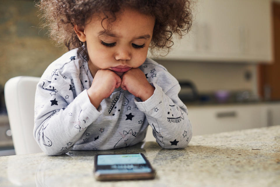 Toddler girl using a smartphone sat at the kitchen table.