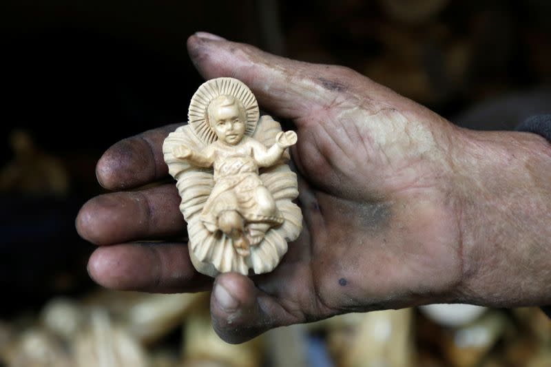 Palestinian worker holds a figurine carved from olive wood, to be sold during Christmas season, at a workshop in Bethlehem in the Israeli-occupied West Bank