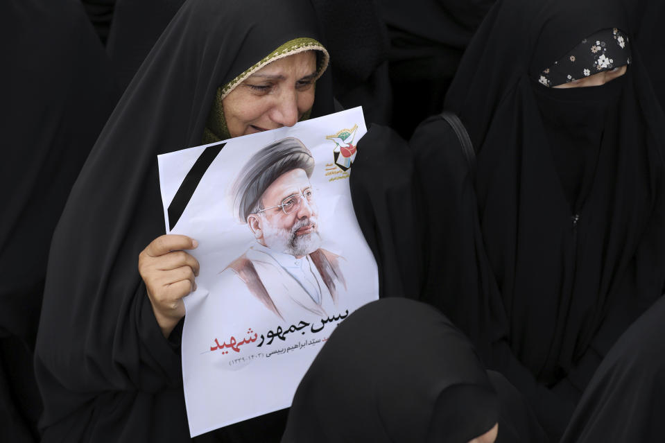 In this photo released by the Iranian Presidency Office, a woman mourns as she holds a poster of President Ebrahim Raisi in a funeral ceremony for him and his companions who were killed in a helicopter crash on Sunday in a mountainous region of the country's northwest, in the city of Tabriz, Iran, Tuesday, May 21, 2024. The sign in the poster reads in Farsi: "Martyr President" (Iranian Presidency Office via AP)