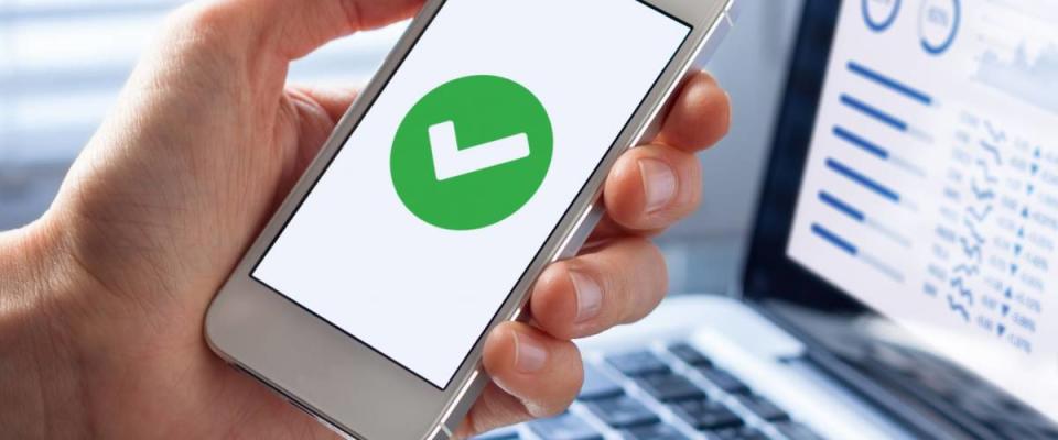 Hand holding a smartphone with a green checkmark icon on the screen to show a validated, confirmed, completed or approved status