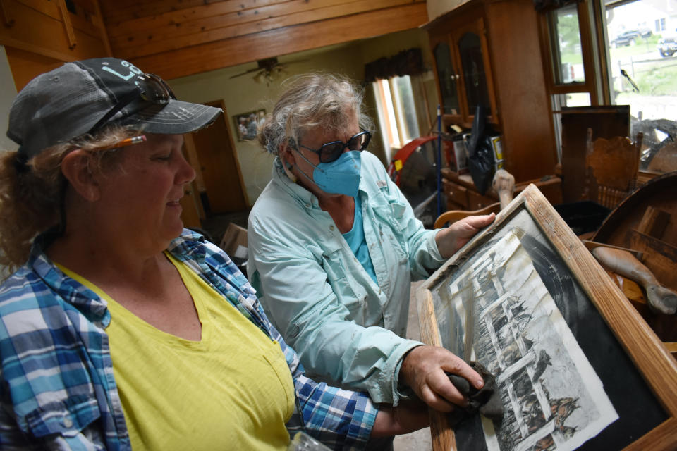 Melody Murter, right, wipes mud from a lithograph by Lindi O'Brien, left, Friday, June 17, 2022, that was partially submerged when floodwaters swamped O'Brien's neighborhood in Fromberg, Mont. Floodwaters that led to widespread damage in Yellowstone National Park caused their most severe impacts in communities outside the park. (AP Photo/Matthew Brown)