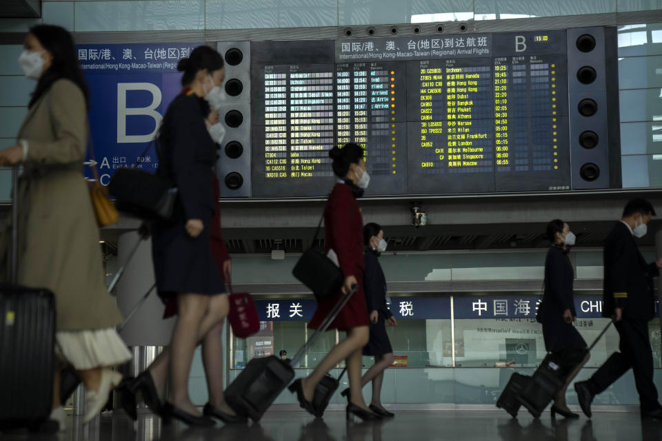 Travelers and airport workers walk past a sign showing international flight arrivals at Beijing Capital International Airport in Beijing, Wednesday, April 26, 2023. Travelers entering China will no longer need to provide a negative PCR test result starting from Saturday, in another easing of China's "zero-COVID" policies. (AP Photo/Mark Schiefelbein)