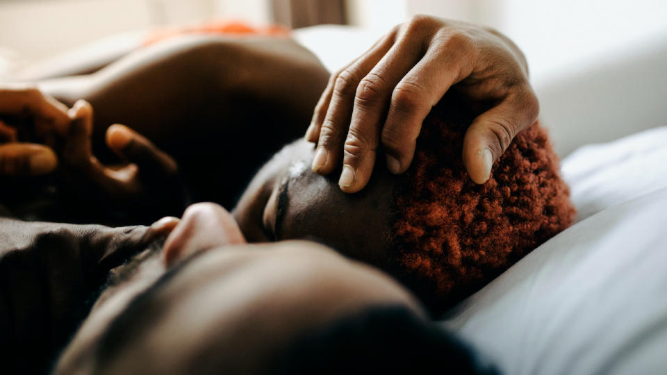 A man snuggles a woman and holds her head in bed