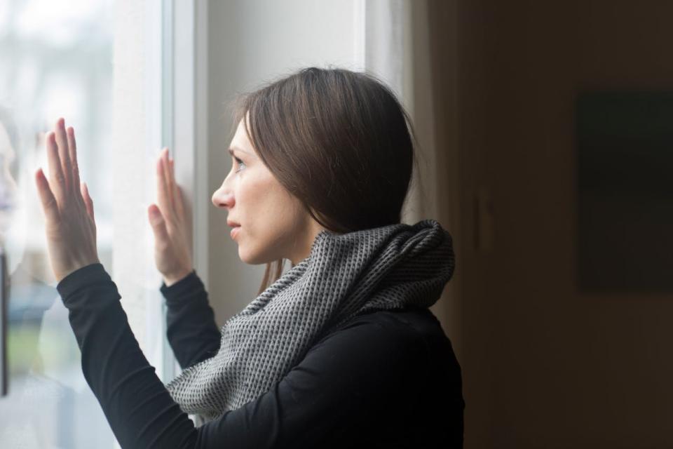 A woman presses her hands to the glass as she looks out a window