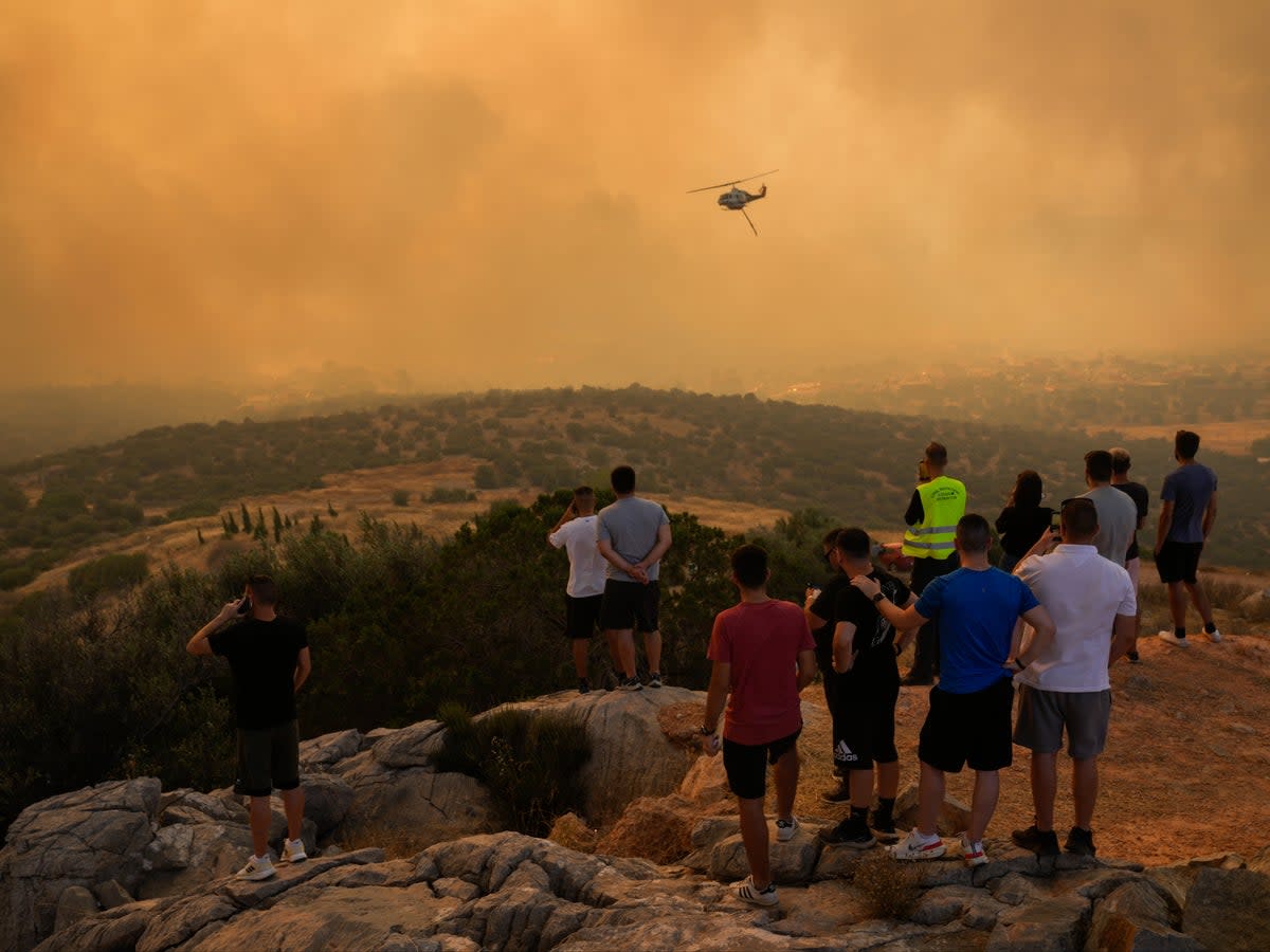 A firefighting helicopter flies through smoke as people look on in Mandra, west of Athens (AP/Petros Giannakouris)