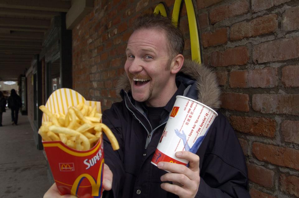 Morgan Spurlock smiling and holding McDonald's fries and drink