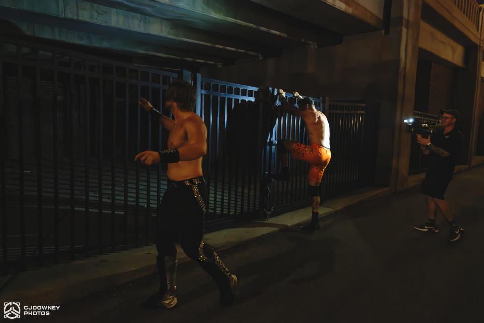 Dirty Dango looks to escape from his opponents by climbing the gate beneath the Jackson Avenue ramps in the Old City. This match, scheduled as a traditional tag-team match, took a turn when the wrestlers were forced to improvise outside during a mask malfunction.