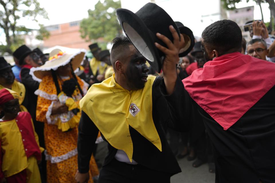 Devotos, vestidos con ropas coloniales y pañuelos que representan los colores de partidos políticos de esa época y con las caras pintadas de negro, participan en la popular fiesta de la Parranda de San Pedro en Guatire, Venezuela, el jueves 29 de junio de 2023. (AP Foto/Ariana Cubillos)