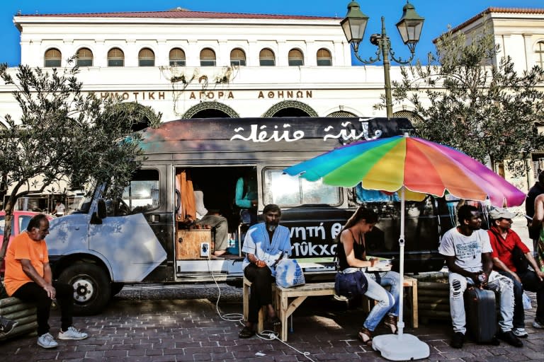 People sit outside a library van in central Athens, one of the initiatives in Greece to offer reading and books to the tens of thousands of refugees stranded in the country