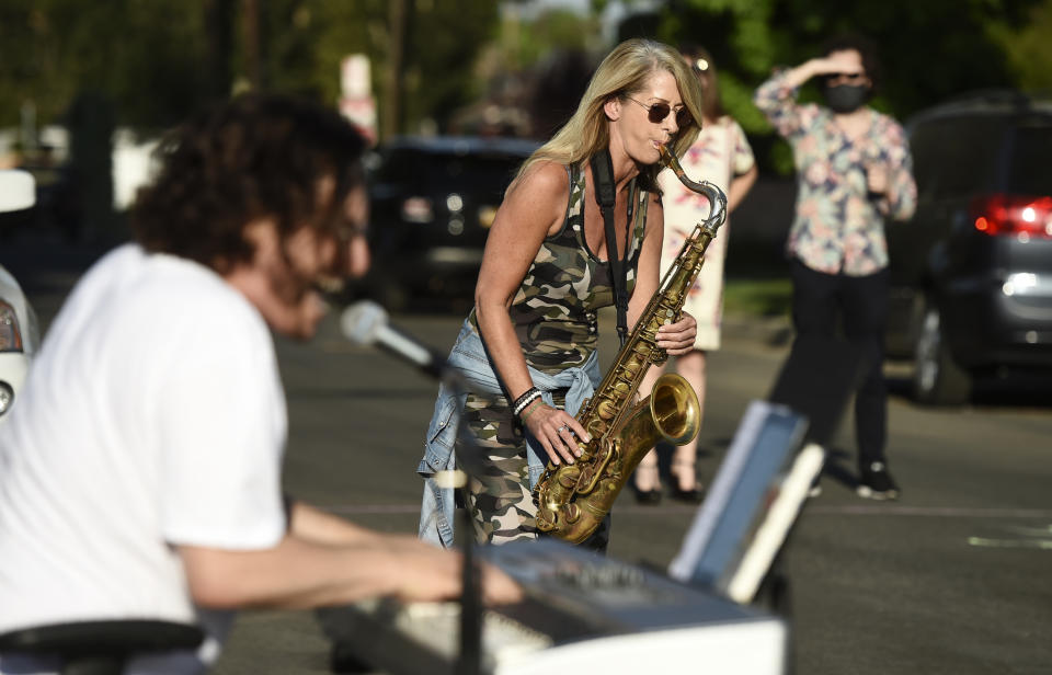 In this May 9, 2020 photo, musician Adam Chester, left, is joined by saxophonist Katja Rieckermann during his weekly neighborhood concert in the Sherman Oaks section of Los Angeles. Normally, Chester is a surrogate Elton John, who sings and plays the rock superstar's parts at rehearsals. With that work on hold, Chester has been giving concerts to his neighbors from a safe social distance in front of his house. Rieckermann is the saxophonist in singer Rod Stewart's band. (AP Photo/Chris Pizzello)