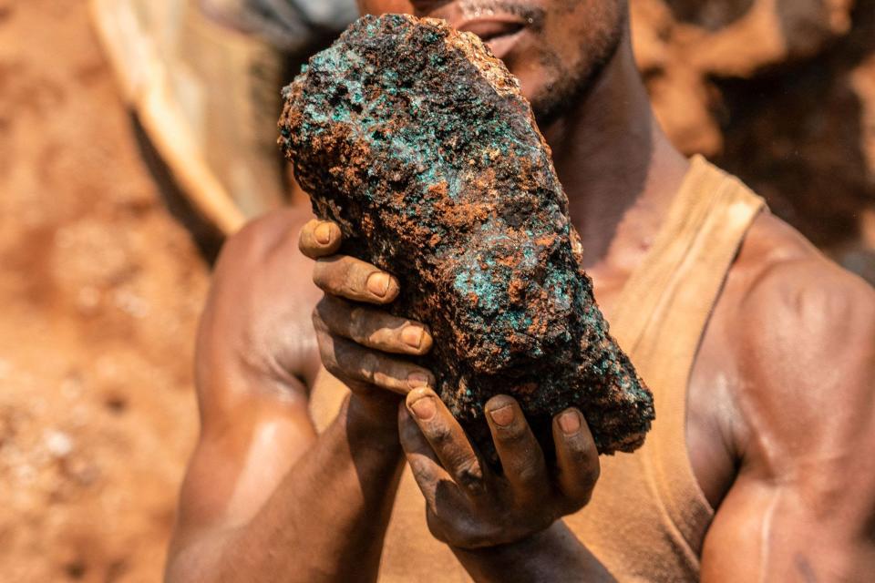 A person in a shirt covered in dust holds up a brown and green stone