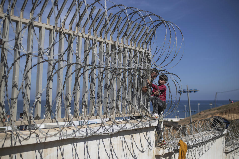 A boy is helped by a man while climbing a fence in the area at the border of Morocco and Spain, outside the Spanish enclave of Ceuta, Tuesday, May 18, 2021. (AP Photo/Mosa'ab Elshamy)