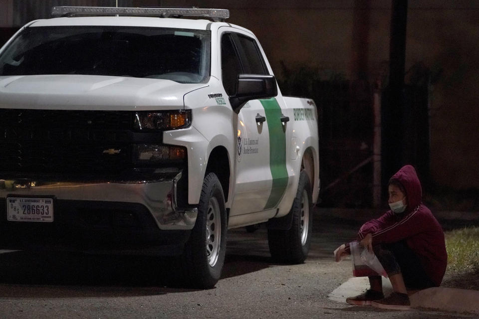 FILE - In this March 24, 2021, file photo, an unaccompanied migrant minor sits next to a U.S. Customs and Border Protection vehicle at an intake area after turning herself in upon crossing the U.S.-Mexico border in Roma, Texas. Confronted with a stream of unaccompanied children crossing the border from Mexico, the U.S. government has awarded shelter-construction and management contracts to private companies that critics say may not be equipped to adequately care for the minors. (AP Photo/Julio Cortez, File)