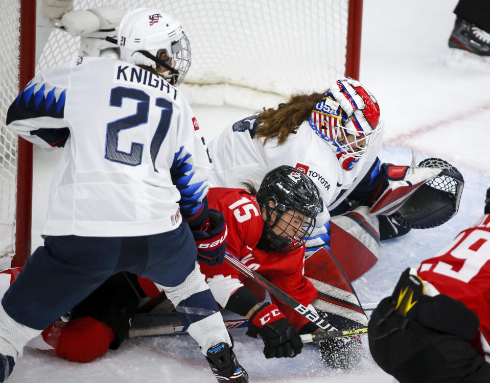 Canada's Melodie Daoust, center, is checked by United States' Hilary Knight, left, against goalie Nicole Hensley during the second period of the IIHF hockey women's world championships title game in Calgary, Alberta, Tuesday, Aug. 31, 2021. (Jeff McIntosh/The Canadian Press via AP)
