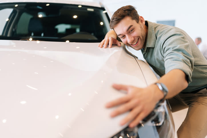 Man smiling and hugging a car, displaying affection, possibly indicative of a strong attachment to the vehicle