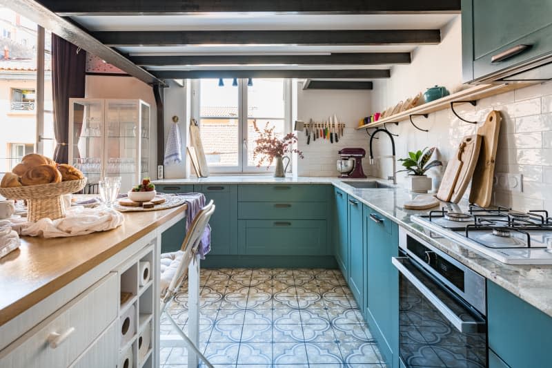 A kitchen with white tiled backsplash and teal cabinets.