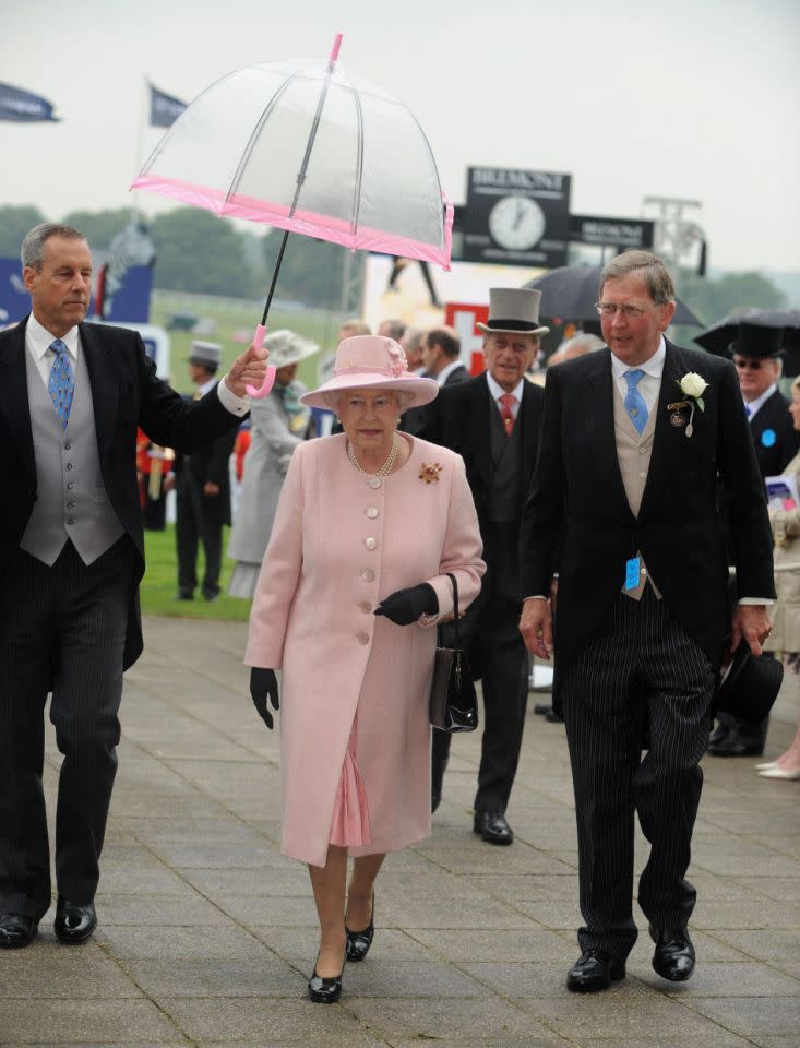 <p>Dank eines Schirmträgers hatte die Queen auf dem Weg zum Pferderennen die Hände frei. Die Monarchin liebt Pferde – und ihre Signature-Schirme. Hier harmoniert ein zartrosa Streifen mit Hut, Kleid und Mantel. (Bild: PA) </p>