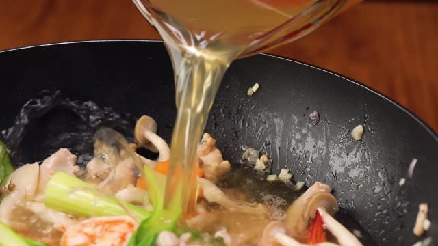 Pouring chicken stock into a pan of stir fried ingredients