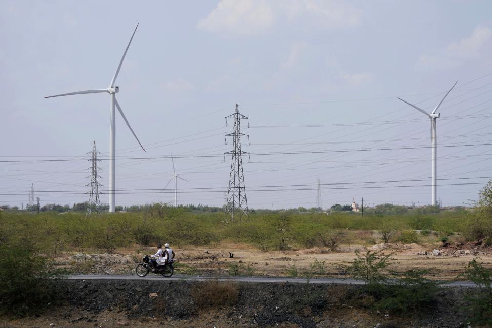 A motorcyclist ride past wind turbines, an Adani Group project, near Sadla village in Surendranagar district of Gujarat state, India, Monday, March 20, 2023. Gautam Adani and his companies lost tens of billions of dollars and the stock for his green energy companies have plummeted. Despite Adani's renewable energy targets accounting for 10% of India's clean energy goals, some analysts say Adani's woes won't likely hurt India's energy transition. (AP Photo/Ajit Solanki)