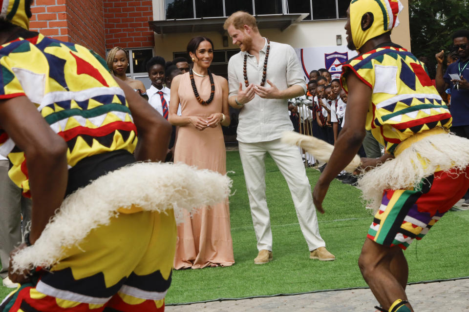 Prince Harry and Meghan Markle watch traditional dancers perform, both smiling and clapping
