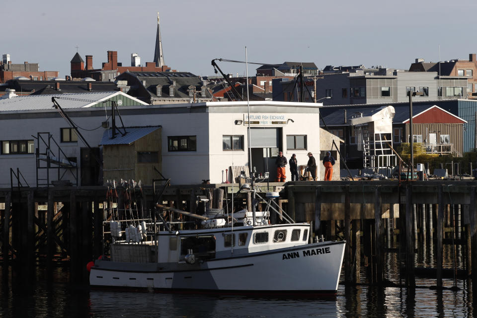 FILE - This March 25, 2020, file photo shows workers gathered outside the Portland Fish Exchange after unloading fish in Portland, Maine. On this day just one boat brought in a load of fish. The amount of commercial fishing taking place worldwide has dipped since the start of the coronavirus pandemic. (AP Photo/Robert F. Bukaty, File)