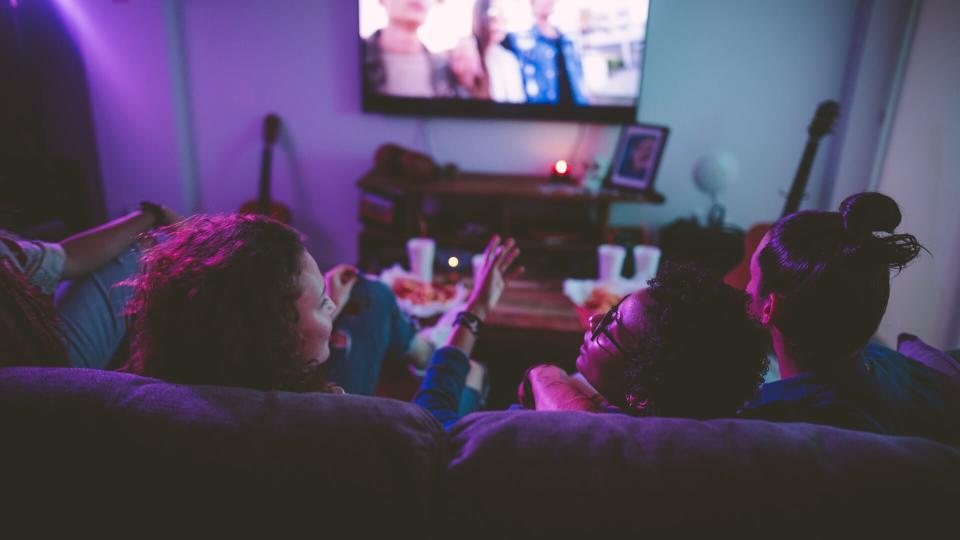 Young multi-ethnic hipster friends relaxing on living room sofa and watching film on TV.