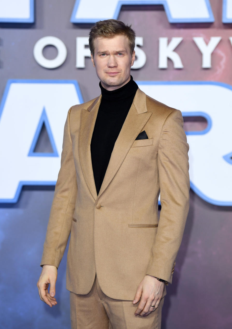 Joonas Suotamo poses on the red carpet in a beige suit with a black turtleneck at an event for "Star Wars: Rise of Skywalker"