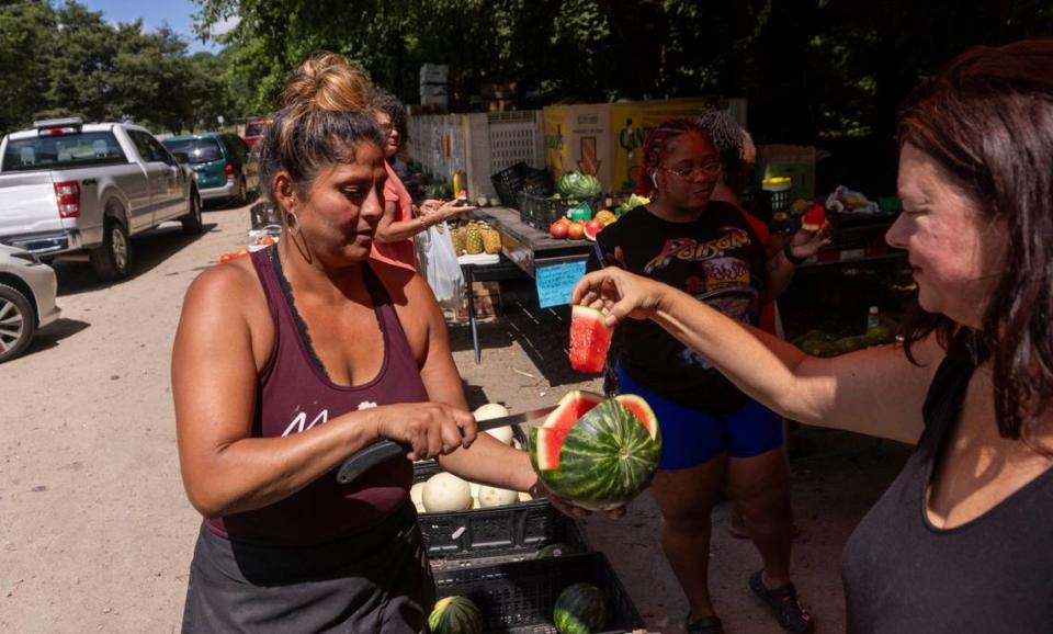 Sanjuana Sanchez, known as the “Watermelon Lady,” offers Angel Coursen a sample of fresh watermelon from her stand on New Bern Avenue in Raleigh, Thursday, June 20, 2024. Sanchez saw an uptick in watermelon and fresh fruit sales Thursday as the Triangle experienced a heat wave.